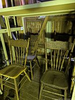 Four wooden pressed-back chairs in storage