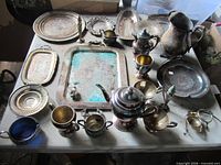 Overhead view showing multiple tarnished silverplate trays, coffee pot, pitcher, goblets and accessories on table