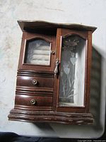 Front view of wooden jewelry cabinet showing drawers, glass panels, etched floral door
