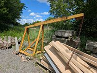 Full view of yellow steel forklift boom attachment with chain at end, stacked lumber and logs nearby
