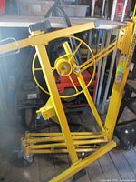 Folded yellow drywall lift showing crank wheel, legs and mast