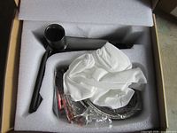 Box opened showing gunmetal faucet, hoses, white protective cover and foam insert