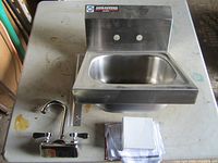 Stainless steel hand sink with backsplash, faucet, bracket and paperwork on table