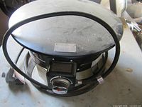 Overall view of black steel Outland Firebowl with hose and control knob visible