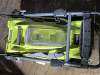 Top view of Ryobi lawn mower showing deck, clear battery lid, folding handle
