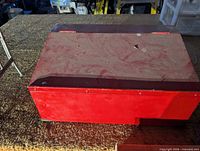 Closed red wooden storage box, dusty top, paint wear