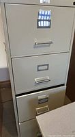Front view of beige four-drawer filing cabinet with one drawer open showing interior depth and condition