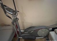 Full view of gray/silver elliptical cross trainer with console, foot pedals and flywheel housing