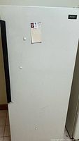 Front view of white Kenmore upright freezer with black handle, showing scratches and dents