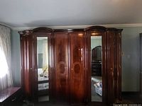 Front view of large dark mahogany armoire showing mirrored outer doors and three central wood doors with carved details