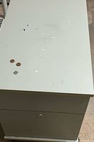 Top and front view showing light gray metal cabinet, two drawers, lock, paint chips