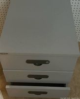 Front view of white 3-drawer nightstand with one drawer open showing recessed metal pulls