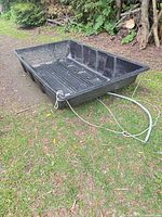 Overall view of black plastic sled with pull rope on grass
