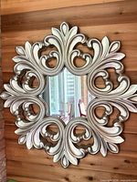 Front view of ornate silver-champagne Baroque round mirror on wood wall
