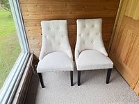Front view of both cream dining chairs showing upholstery, tufting, legs