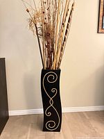 Full view of tall black vase with gold accent and dried stems