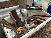 Large assortment of kitchen knives, cleaver, kitchen shears, and honing steel in a white cooler bin.