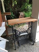 Full view of vintage Singer sewing machine base with wooden top placed outdoors.