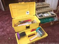Yellow plastic toolbox with various craft supplies including tools and beads inside, and a wood stand with multiple compartments in background
