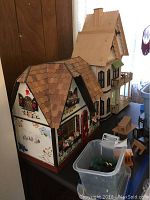 Two doll houses, one painted with cottage decorations and the other plain wood, set on a table with some doll house furniture around.
