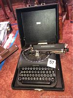 Photo showing Remington Rand black typewriter in open black carrying case, vintage mechanical keys visible.