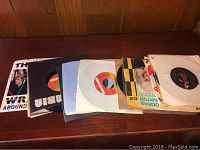 Image of a collection of 7-inch 45 RPM vinyl records laid out on a wooden surface, showing various colorful sleeves and vinyl records.