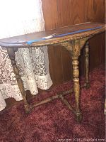 Full view of the oval wooden side table with turned legs and stretchers, placed on a red carpet near lace curtains.