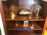Shelf with various sizes of glass dome display jars and small decorative items placed on wooden shelving.