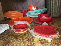 Display of various plates, bowls, and red and orange ceramic dishware on table