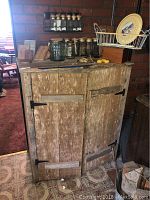 Wide view of rustic wooden cupboard showing two doors, horizontal wood braces, and black metal hinges. The wood has a heavily worn, aged appearance.