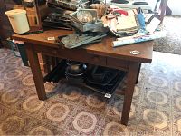 Wooden table displaying assorted kitchenware and household items including baking pans, plastic container, decorative tin, and cast iron pans.