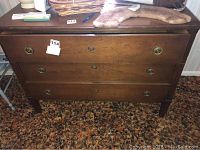 Front view of wood dresser showing three drawers with round brass handles and some items on top.