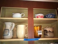 Display of pitchers, ceramic bowls, glass jar, and ceramic jar on wooden shelves