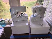 Both Michley double stitch portable sewing machines placed on their respective boxes near window.