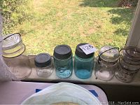 Seven mason jars arranged on a windowsill, displaying sizes and colors