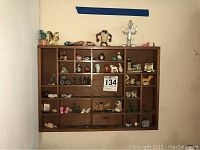 Wooden shelf mounted on wall filled with various small figurines and decorative items including animals and other collectibles