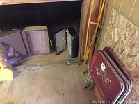 Three vintage items: two open vintage suitcases and one closed suitcase placed on the floor alongside a long wooden handle or plank.