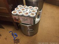 Ten Ball Mason jars with colorful lids on top of a large stainless steel canning pot, with another pot in the background.