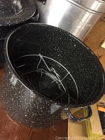 Large black speckled canning pot with metal rack insert inside, showing interior and handles.