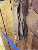 Leather purses and leather straps placed on a wooden wall background, showing wear and textured leather surfaces.