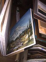 Photo showing side view of stacked canvases including landscape painting of snowy mountain and trees