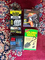 Four boxed items: Alien Tape, MotoMaster Eliminator LED spotlight, MotoMaster ratchet tie-downs, Coghlan's folding shovel