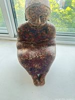 Front view of seated ceramic figure showing mottled reddish finish and overall form