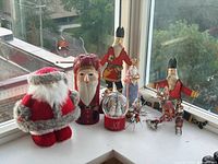 Group view showing plush Santa, three wooden Santas, snow globe, and metal figurines