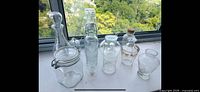 Front view of assorted clear glass bottles, jars and decanters arranged on windowsill