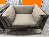 Front view of one chair showing wicker frame, cushion, aluminum legs