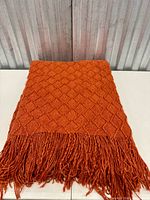 Folded orange diamond-knit blanket showing texture and fringe