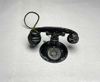 Front view of TootsieToy miniature telephone showing handset on cradle and green cord