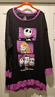 Full view of black long-sleeve top on hanger with purple trim and character graphics