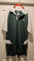 Full front view of green and white Reebok NY Jets polo shirt on hanger